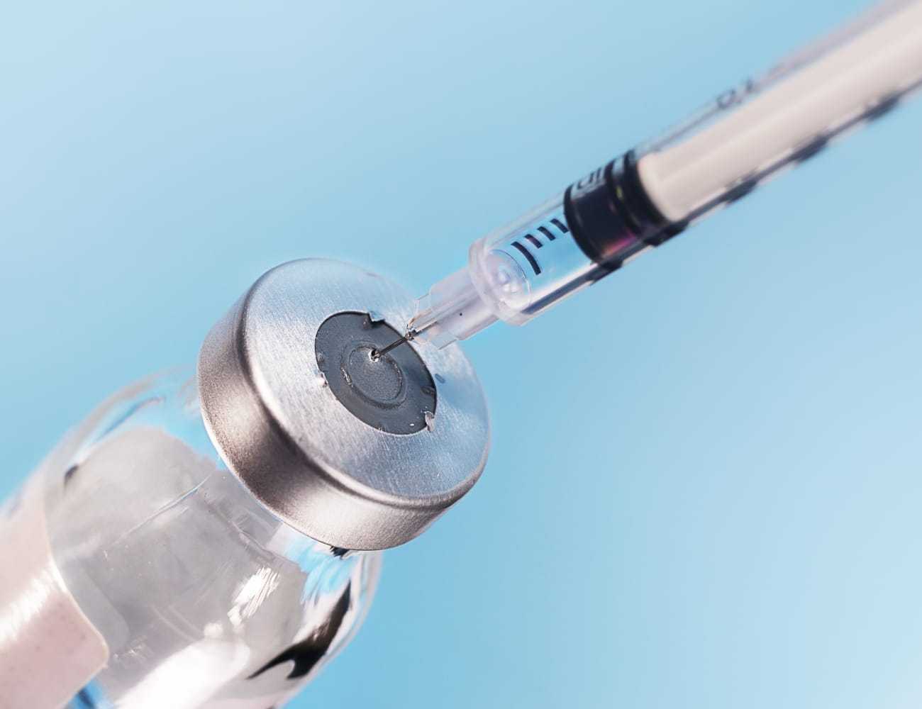 Vaccine vial and syringe with blue background, illustrating medical preparation.