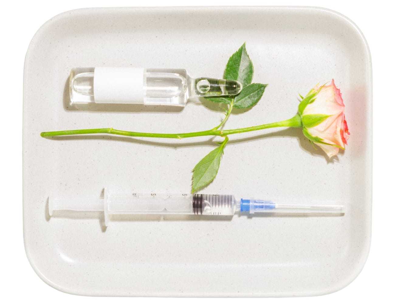 Vial, rose, and syringe displayed on a white tray.