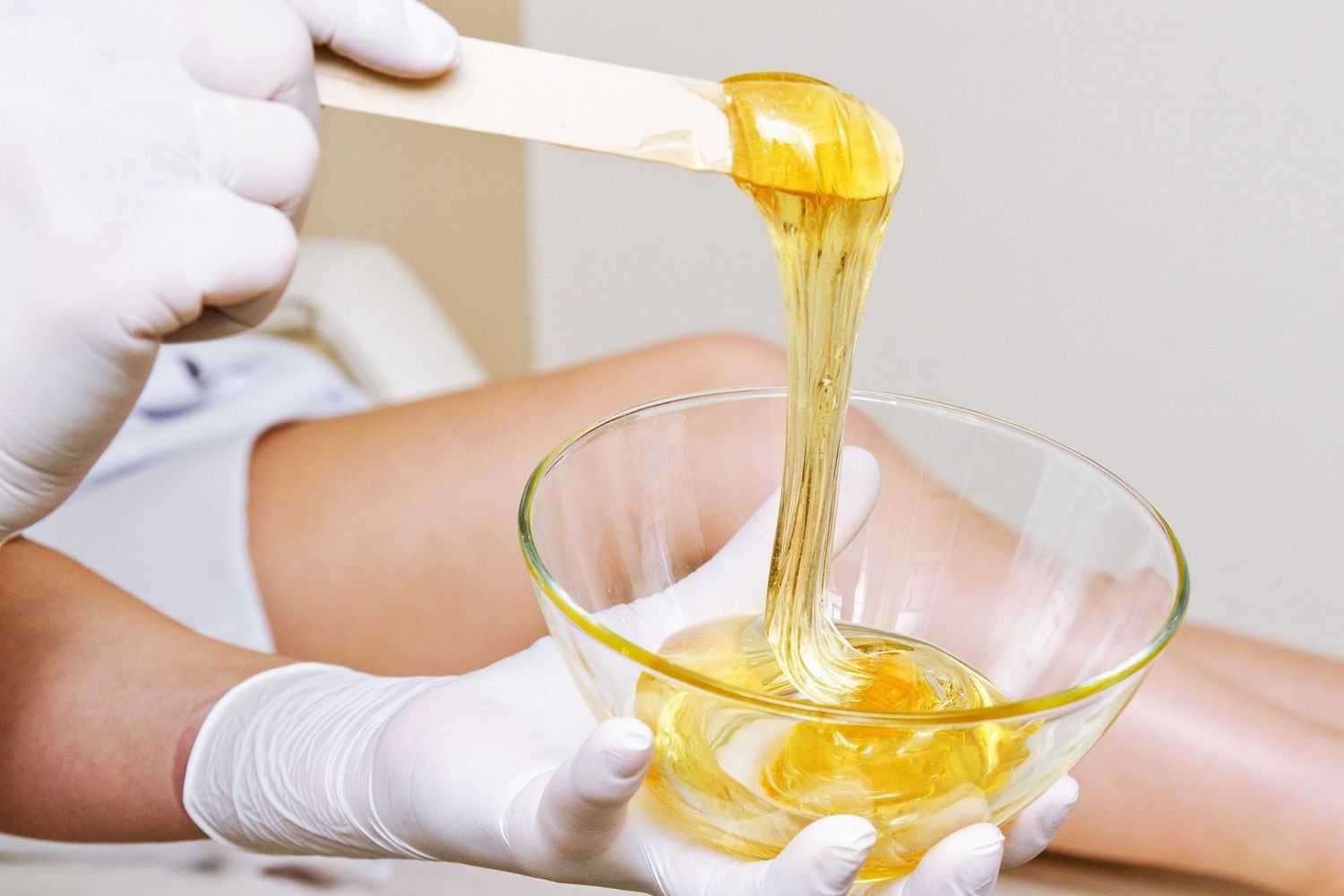 Gloved hands demonstrating the sticky texture of hair removal wax.
