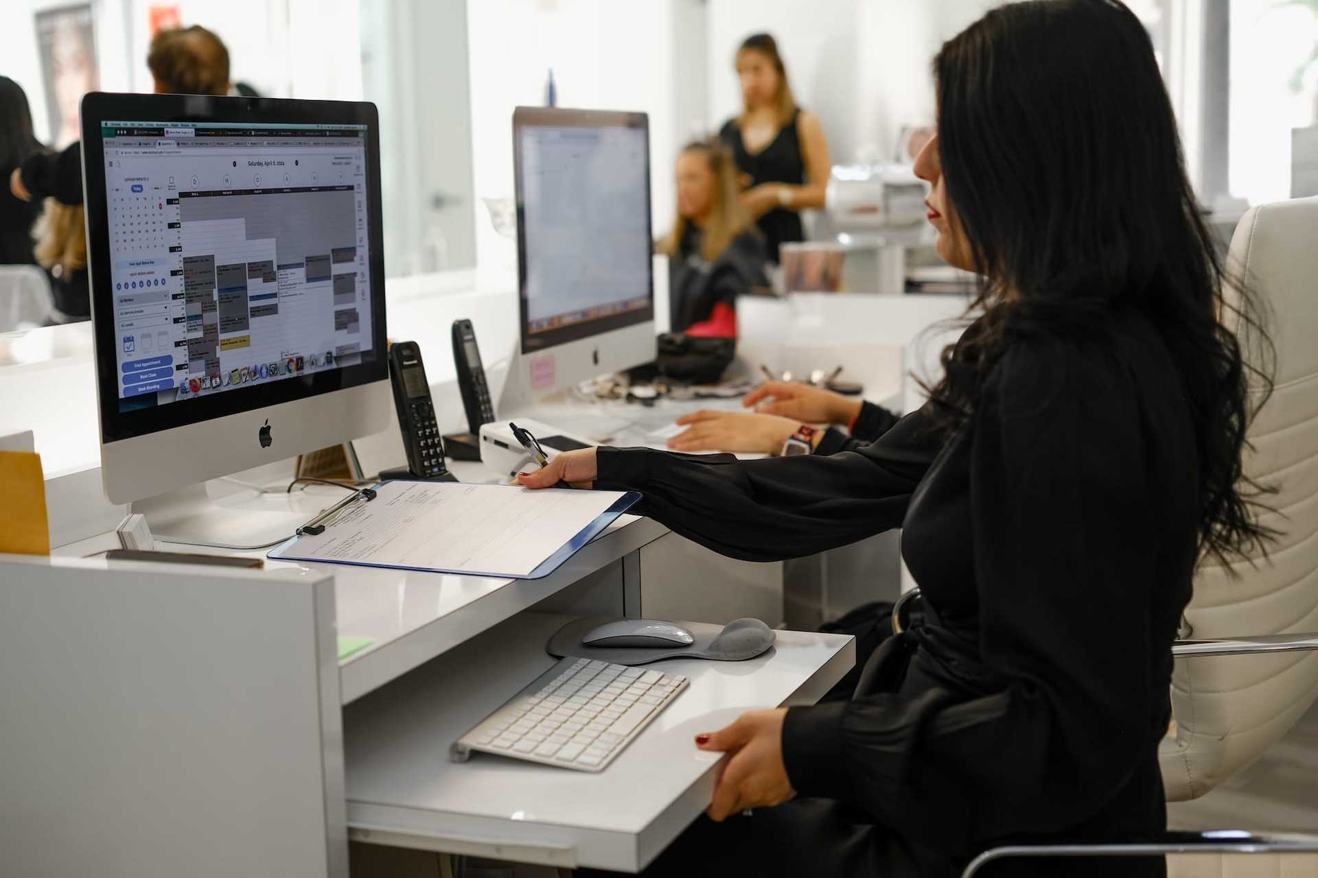 Woman working at a desk with a computer in an office setting.