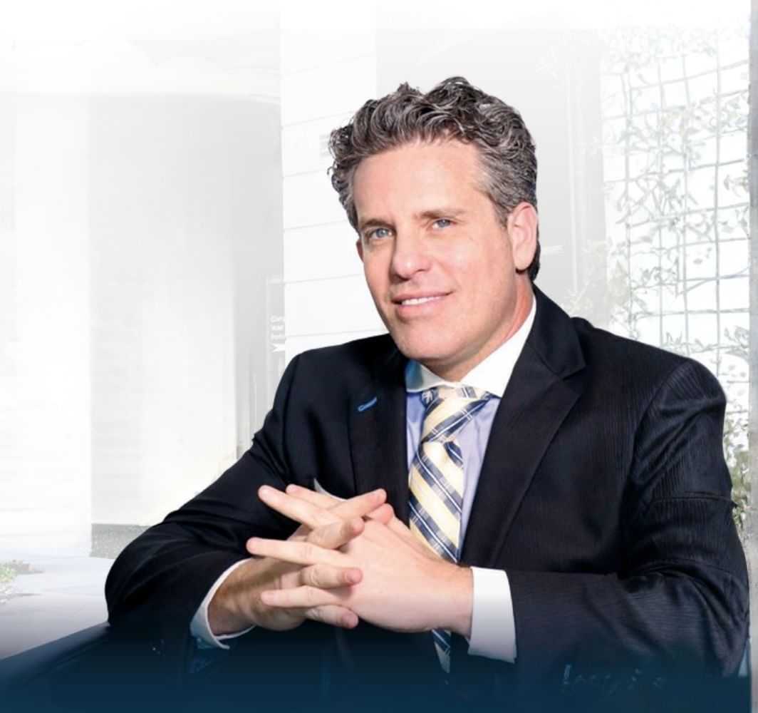 Man in a suit with a striped tie sitting in front of a bright, modern background.