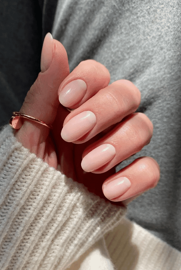 Hand with a gold ring showcasing neatly manicured pastel pink nails.