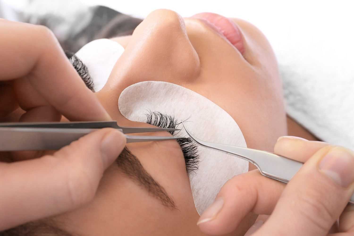 Applying eyelash extensions to a person's closed eye with tweezers.
